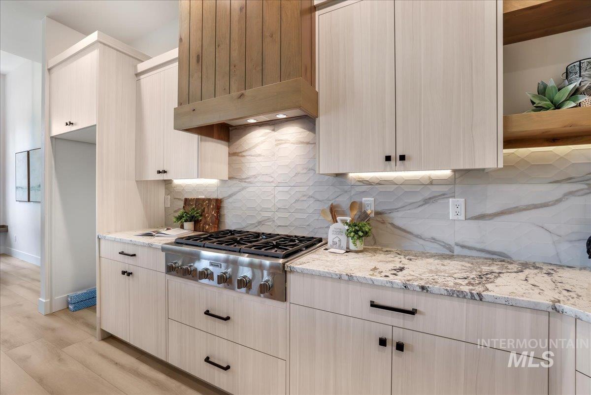 Kitchen with stainless steel gas stovetop, light wood-type flooring, light stone countertops, backsplash, and open shelves