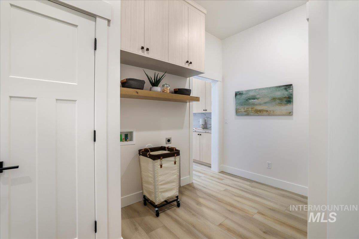 Washroom with electric dryer hookup, light wood-type flooring, cabinet space, and hookup for a washing machine