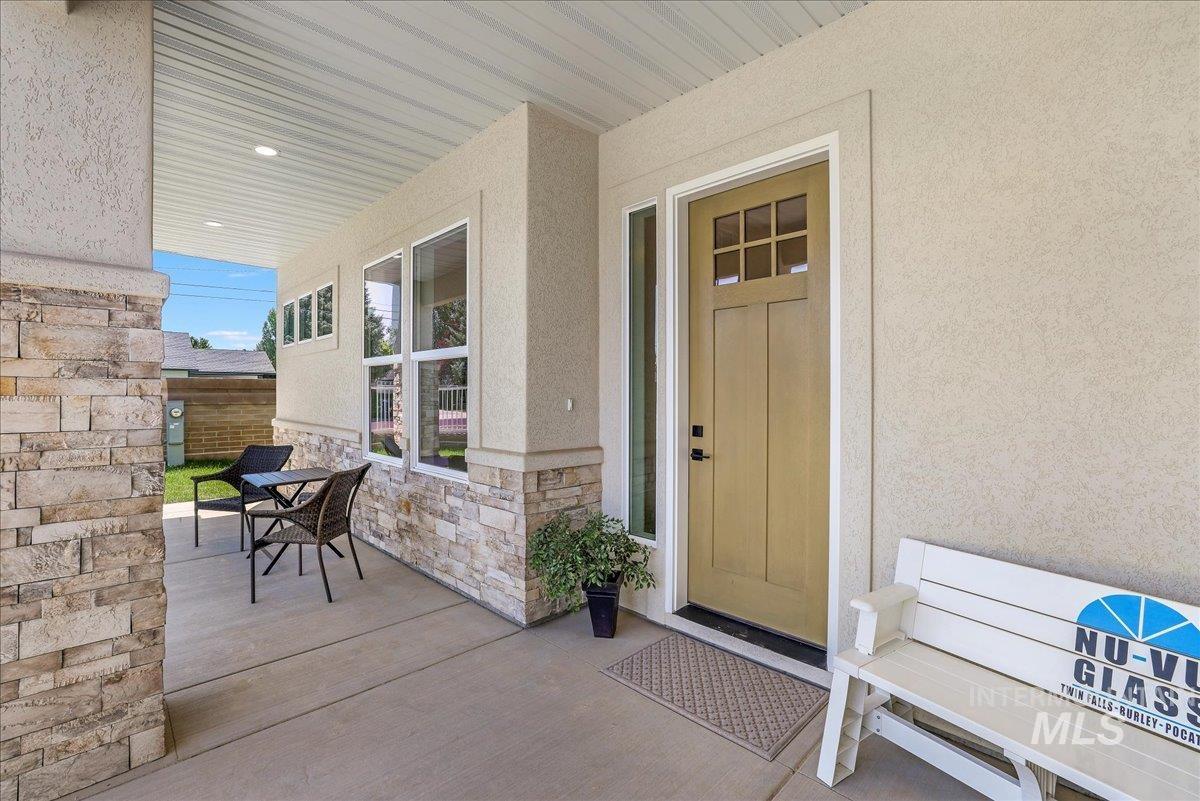 Entrance to property with stucco siding, stone siding, and covered porch