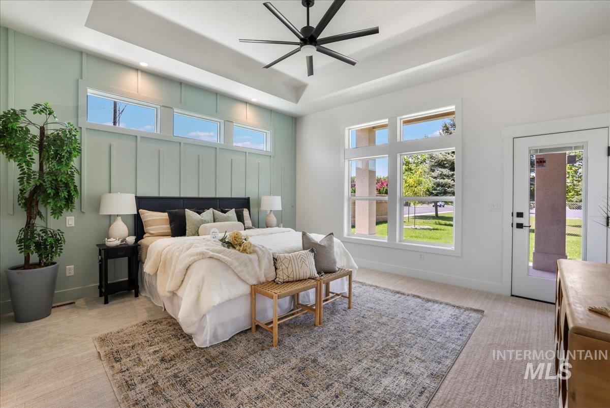 Bedroom with a tray ceiling, light carpet, multiple windows, and access to outside