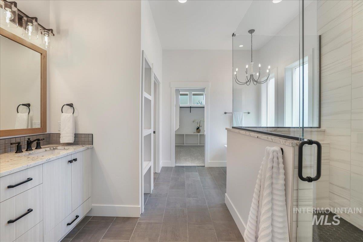 Bathroom featuring a chandelier, a spacious closet, a stall shower, vanity, and tasteful backsplash