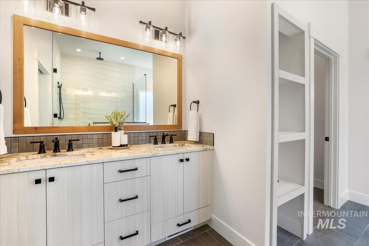 Full bathroom with backsplash, double vanity, a shower stall, and a walk in closet