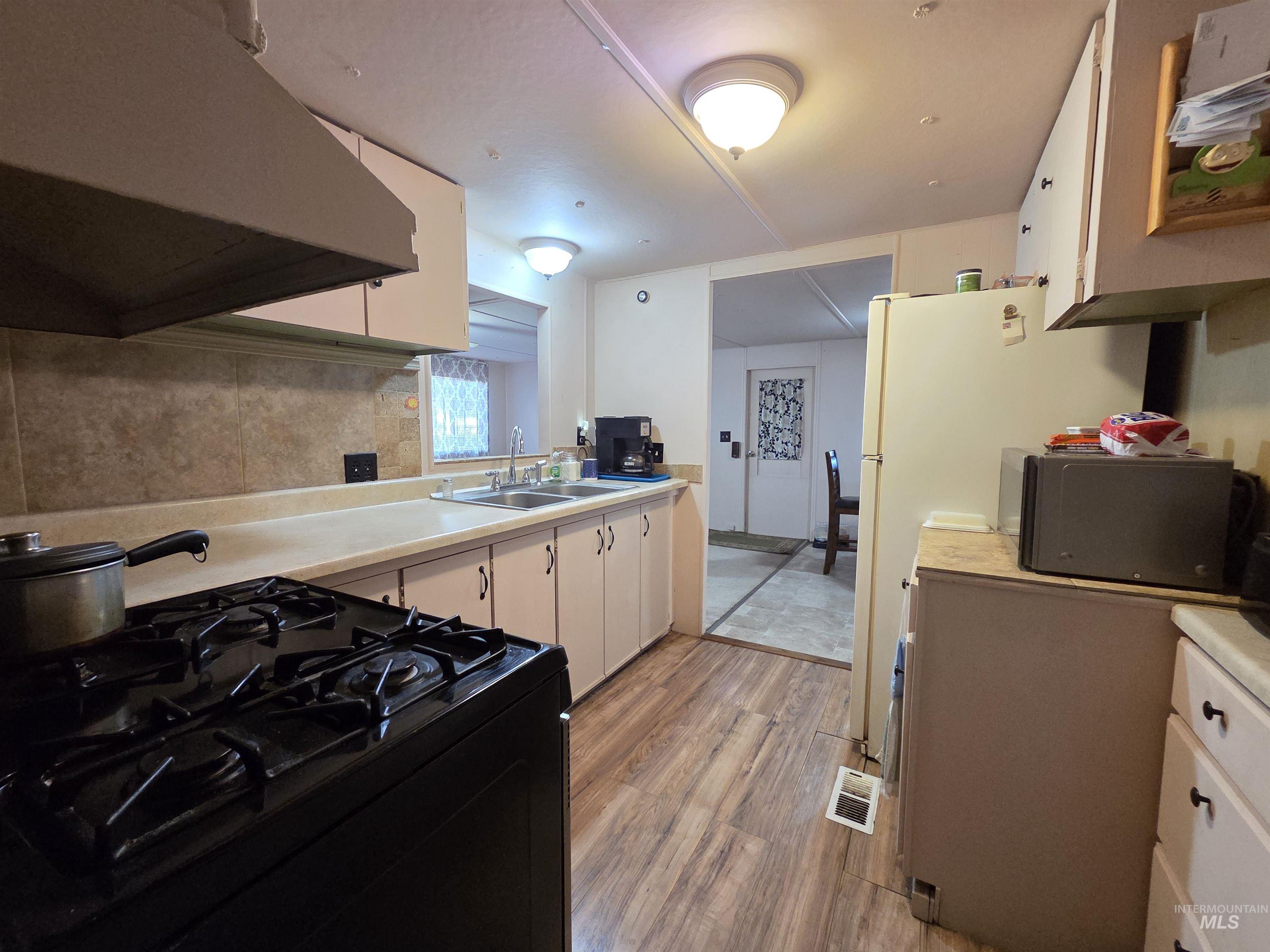 Kitchen with under cabinet range hood, gas stove, light countertops, light wood-type flooring, and white cabinetry
