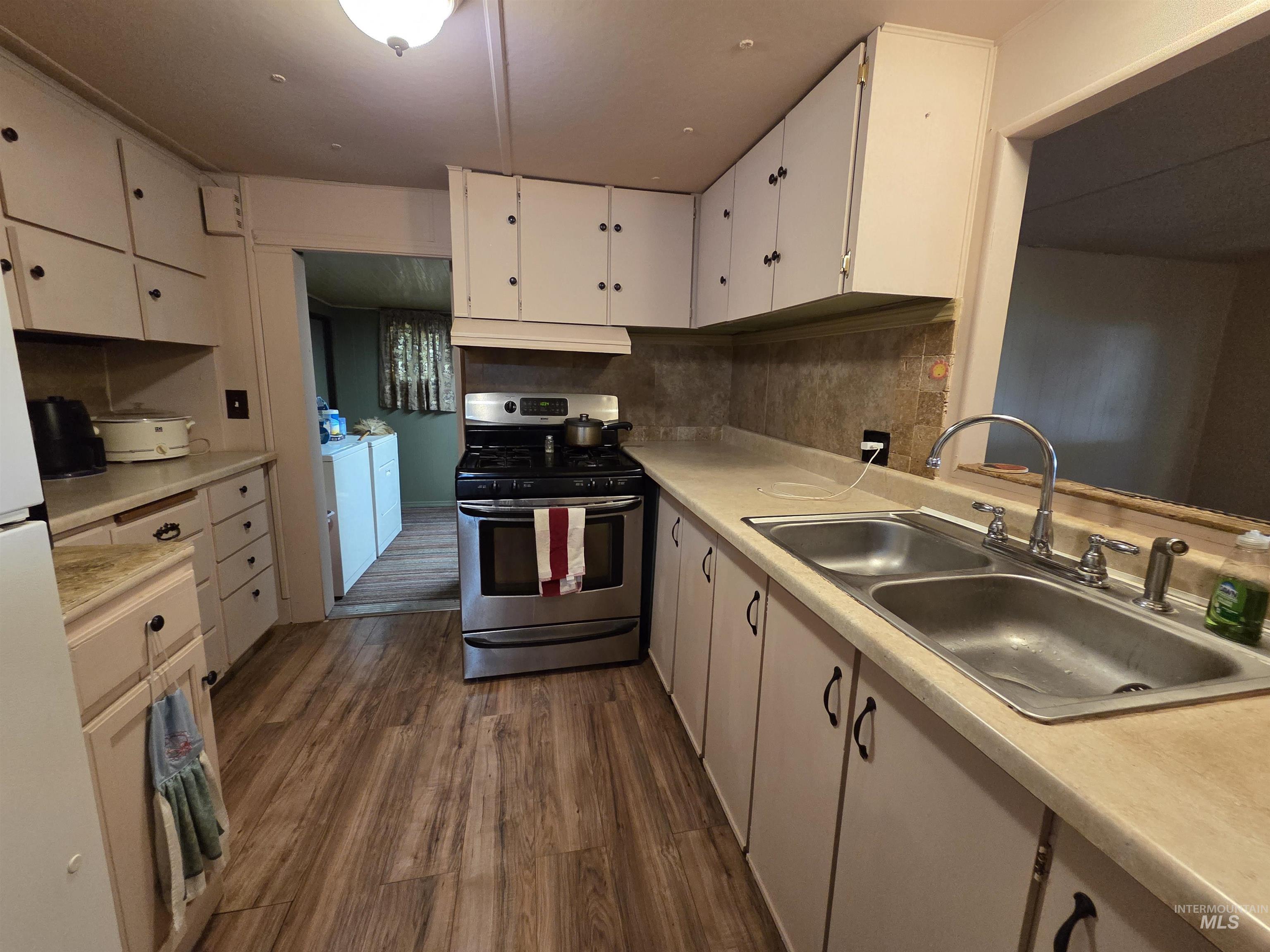 Kitchen featuring stainless steel gas stove, washer and clothes dryer, under cabinet range hood, and light countertops