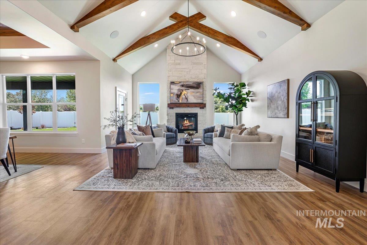 Living room featuring beam ceiling, wood finished floors, healthy amount of natural light, a stone fireplace, and a chandelier