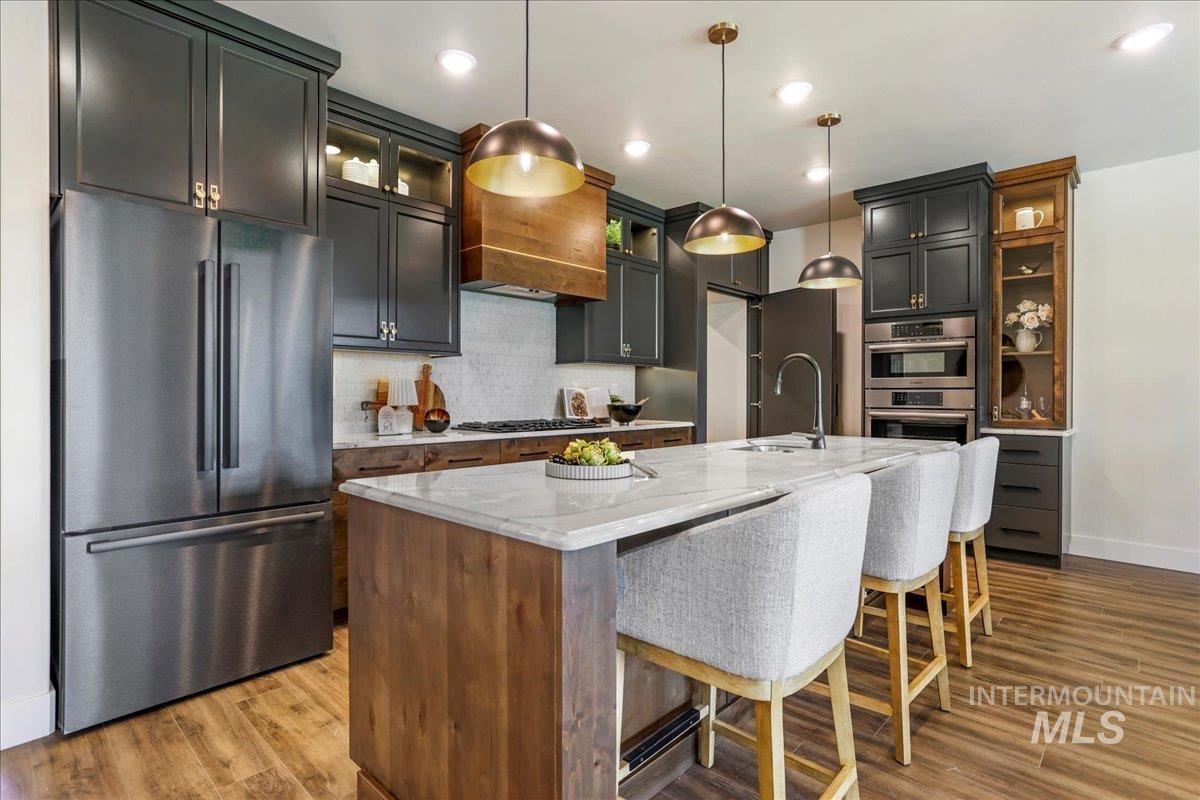 Kitchen featuring stainless steel appliances, light stone counters, backsplash, a kitchen island with sink, and a kitchen breakfast bar