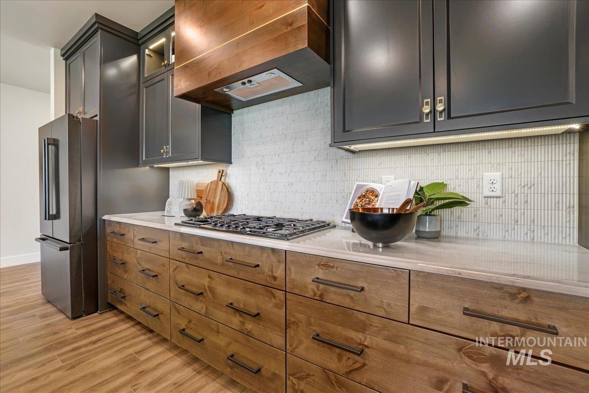 Kitchen with stainless steel appliances, premium range hood, light wood-type flooring, light countertops, and backsplash