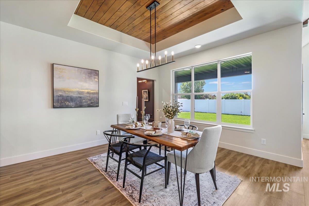 Dining area featuring a raised ceiling, wood ceiling, wood finished floors, and a chandelier