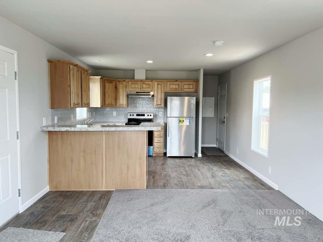 Kitchen featuring appliances with stainless steel finishes, wood finished floors, under cabinet range hood, decorative backsplash, and a peninsula