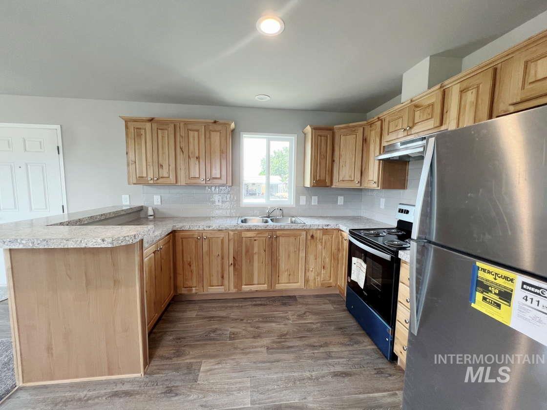 Kitchen with freestanding refrigerator, black / electric stove, light brown cabinetry, a peninsula, and recessed lighting