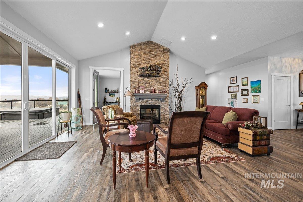 Living area featuring wood finished floors, a stone fireplace, recessed lighting, and high vaulted ceiling