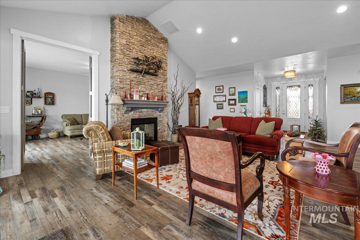 Living room with wood finished floors, a stone fireplace, recessed lighting, and high vaulted ceiling