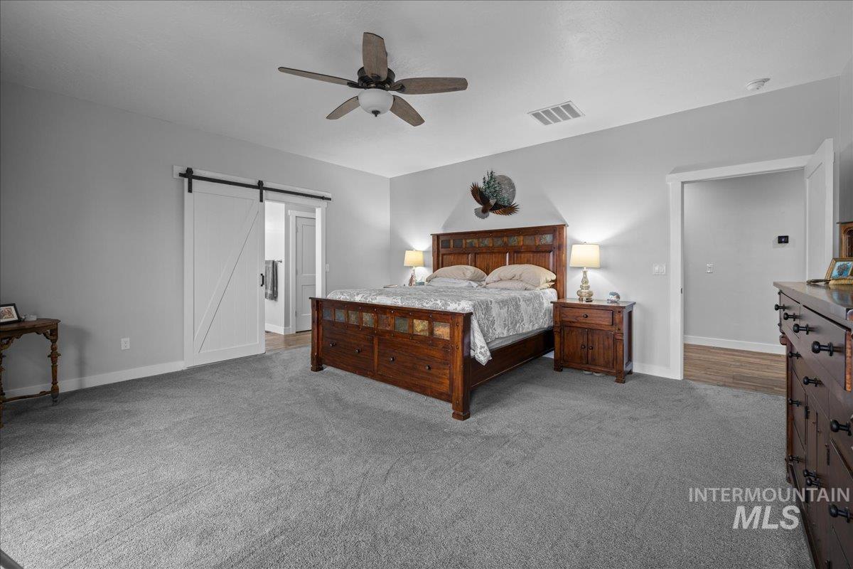 Carpeted bedroom with a barn door and ceiling fan