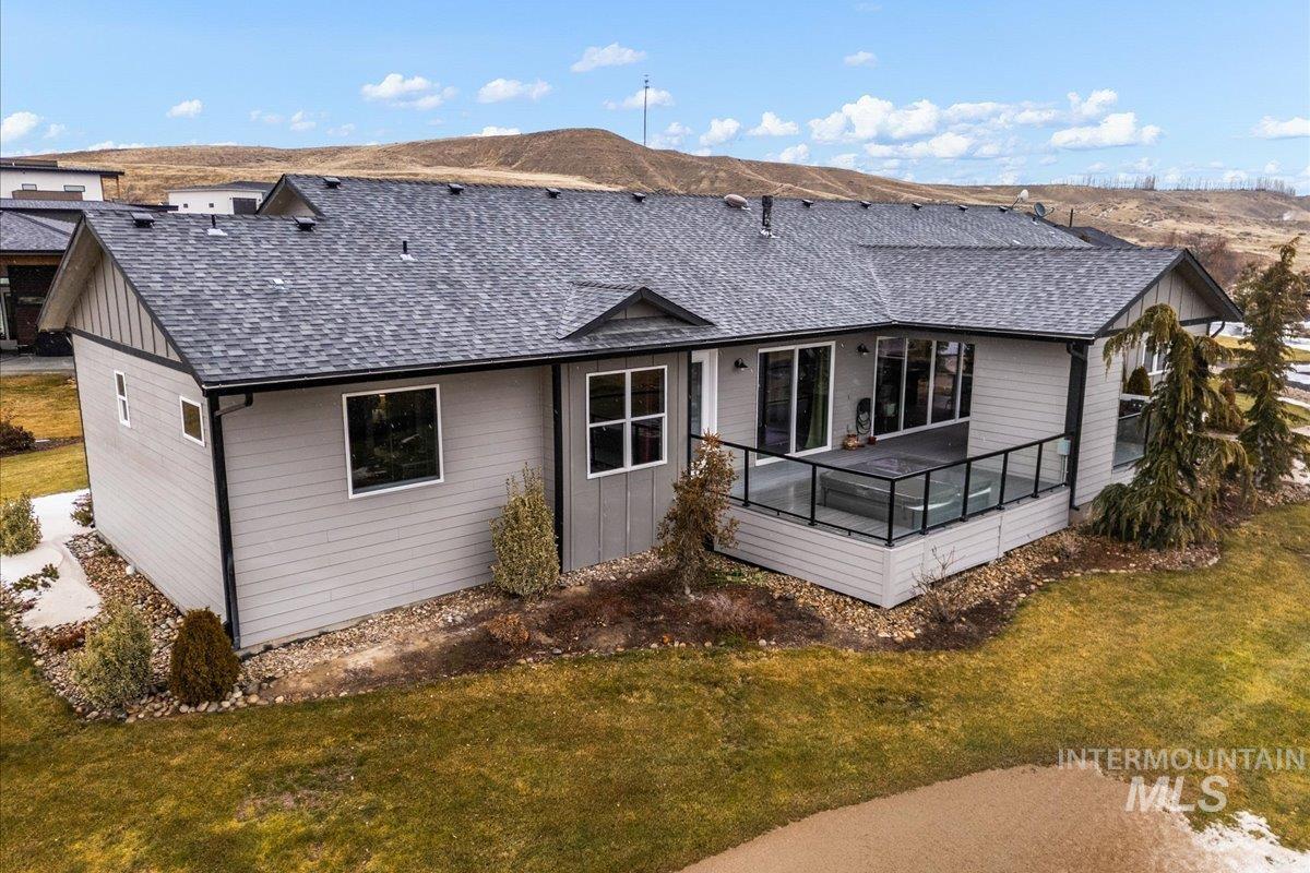 Rear view of property with roof with shingles, a lawn, board and batten siding, and a deck