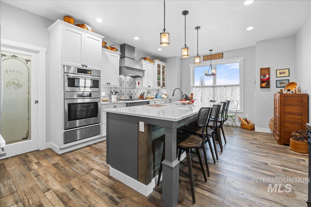 Kitchen with custom exhaust hood, appliances with stainless steel finishes, a warming drawer, light countertops, and hardwood / wood-style floors
