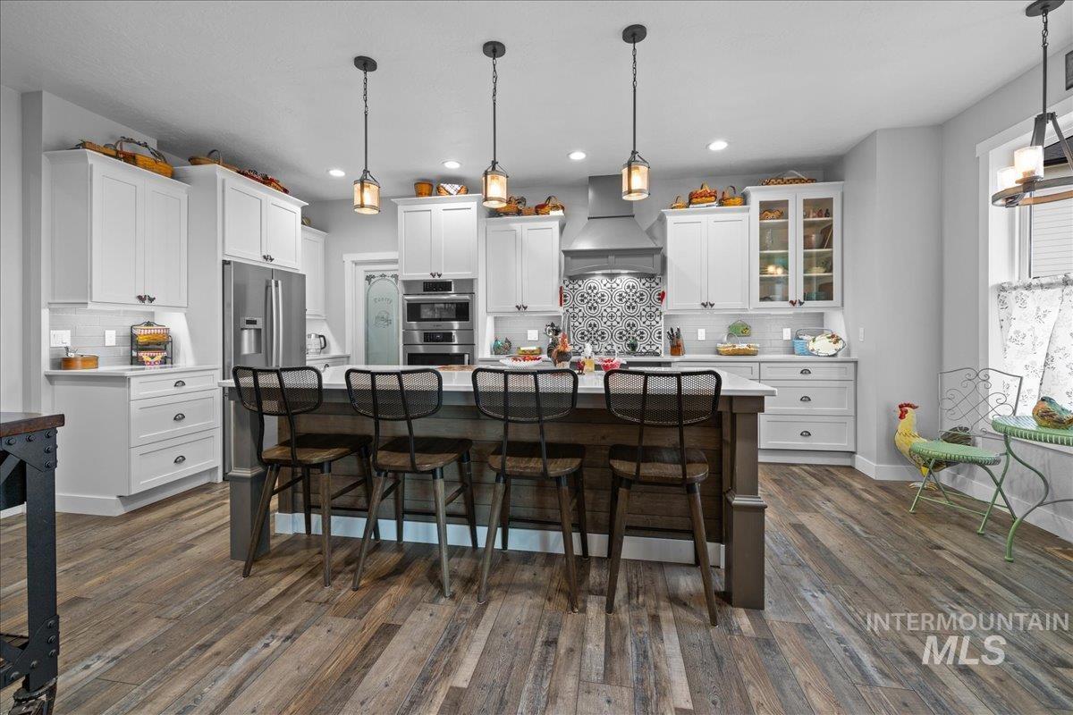 Kitchen featuring wall chimney range hood, white cabinetry, stainless steel appliances, tasteful backsplash, and recessed lighting