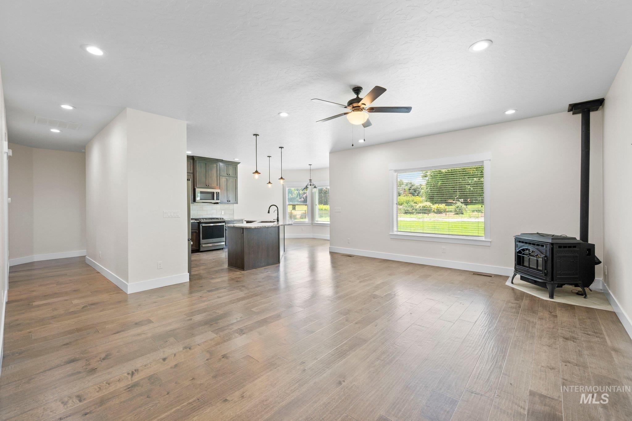 Unfurnished living room featuring a ceiling fan, light wood-type flooring, recessed lighting, and a wood stove
