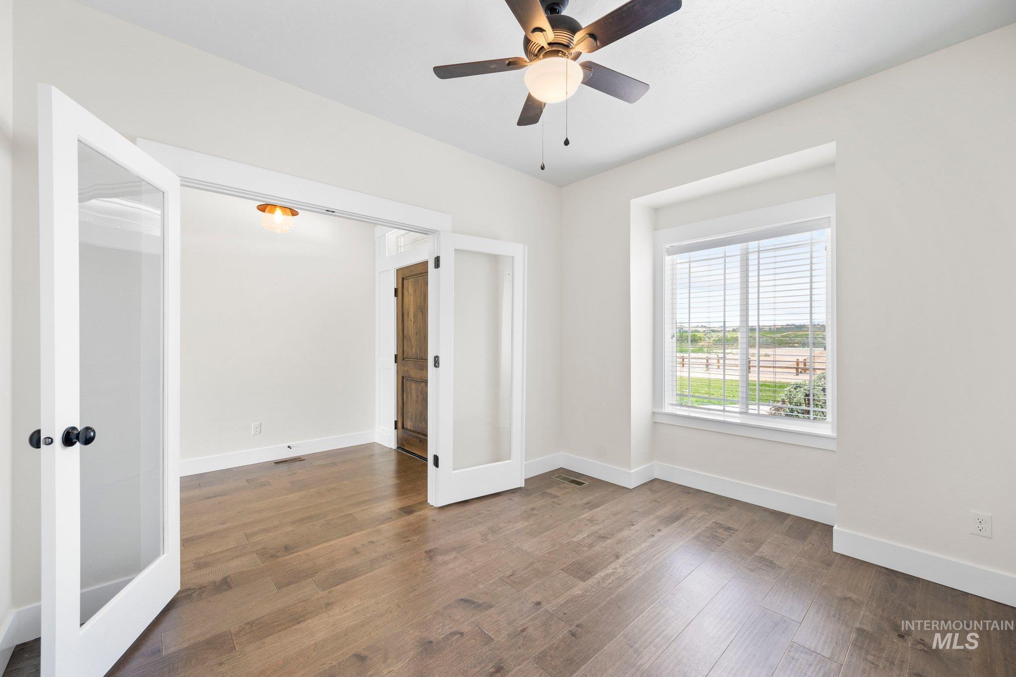 Empty room featuring wood finished floors, a ceiling fan, and french doors