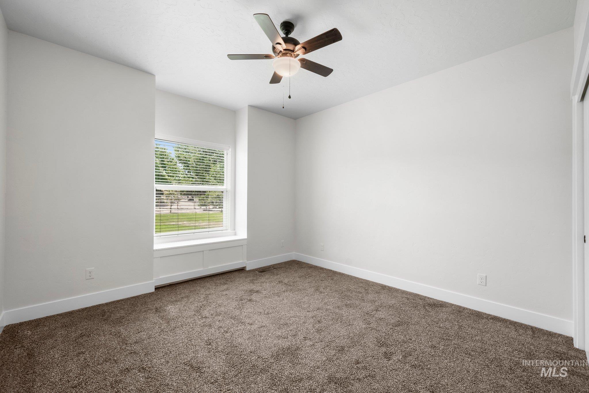 Carpeted spare room featuring baseboards and ceiling fan