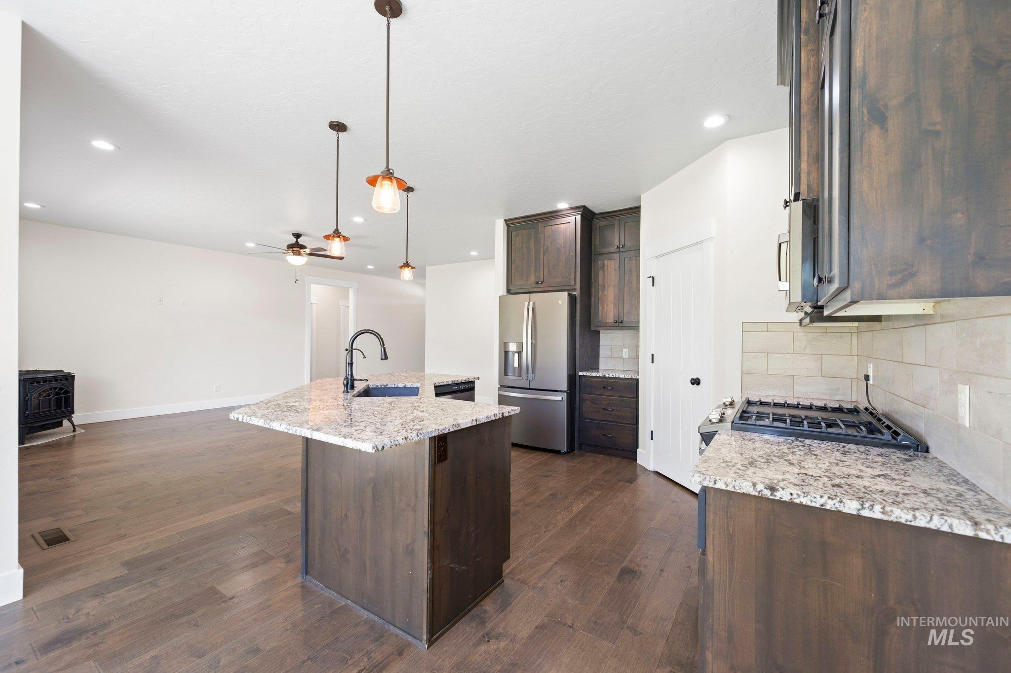 Kitchen with stainless steel fridge with ice dispenser, a wood stove, dark brown cabinetry, tasteful backsplash, and open floor plan