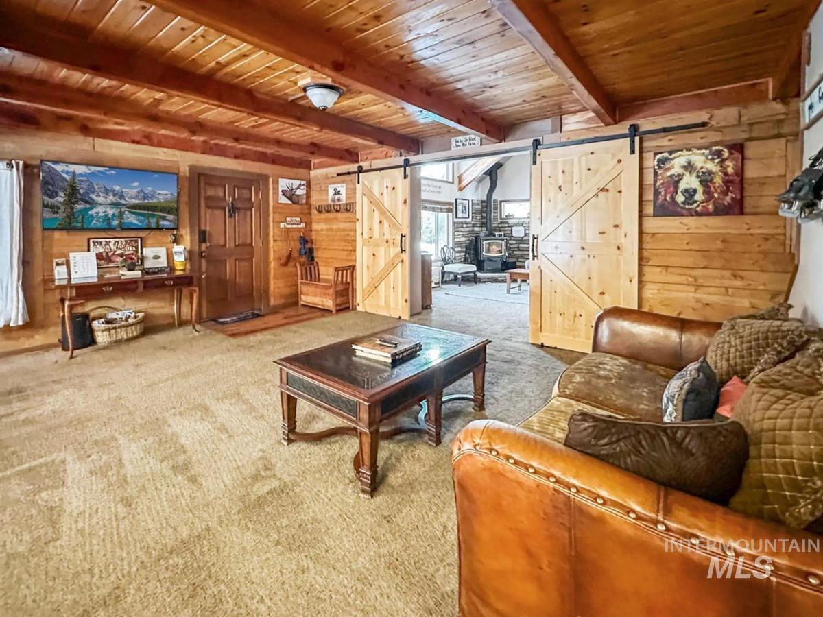 Carpeted living area with a barn door, wooden walls, and a wooden ceiling with exposed beams