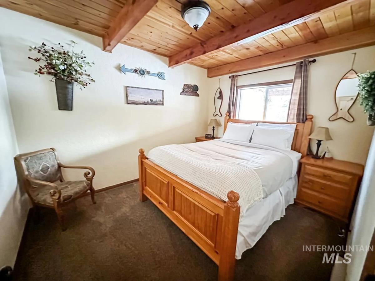 Bedroom featuring a wood ceiling with exposed beams and dark carpet