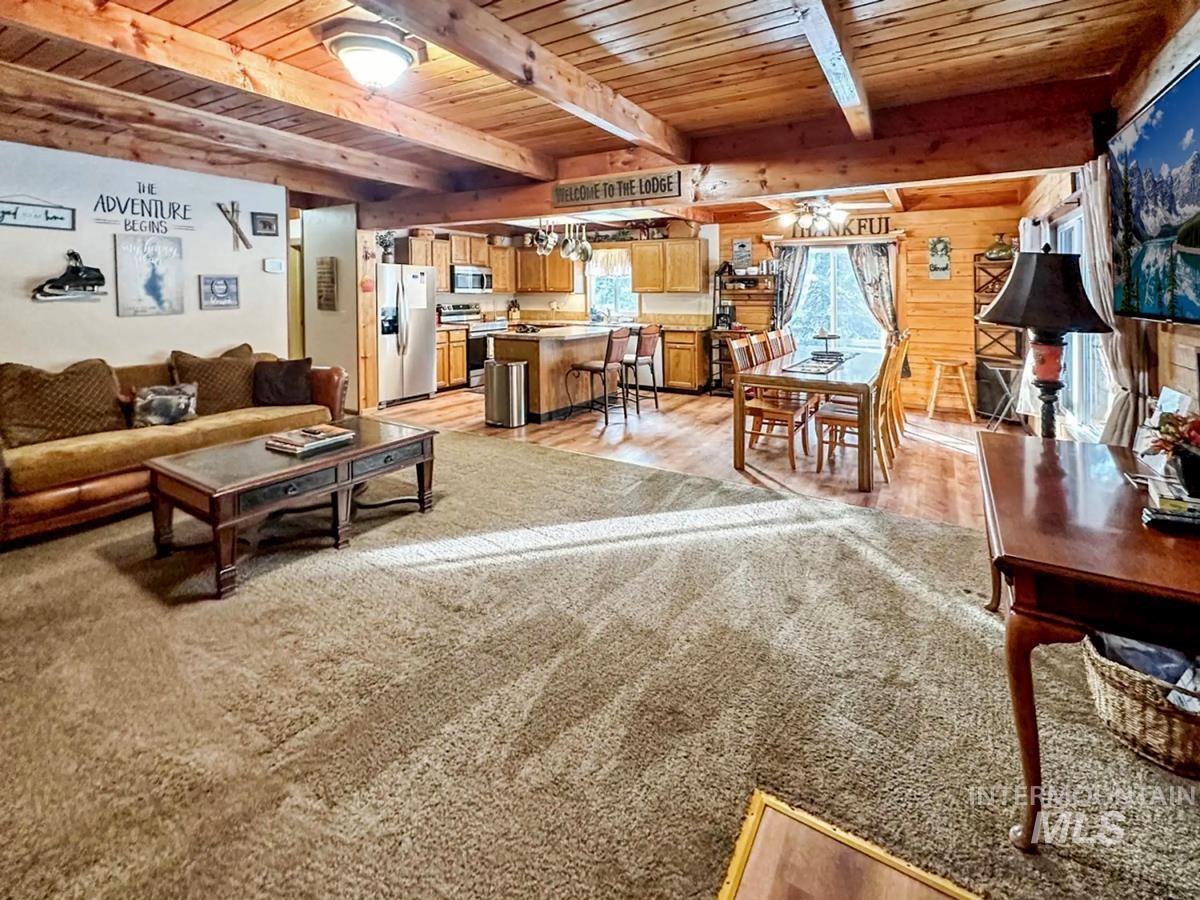 Living area with a wood ceiling with exposed beams, light wood-style flooring, and wooden walls