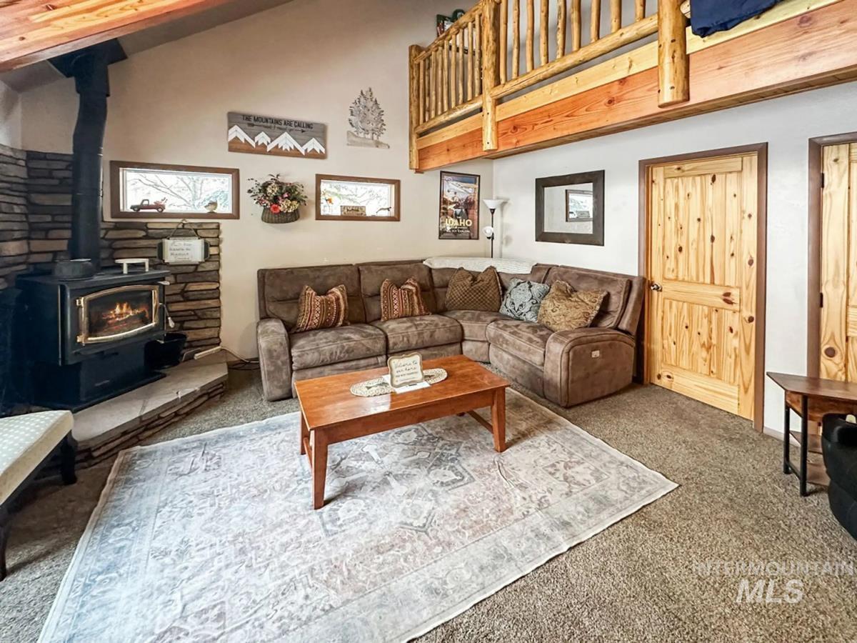 Living room featuring carpet flooring, a wood stove, and lofted ceiling