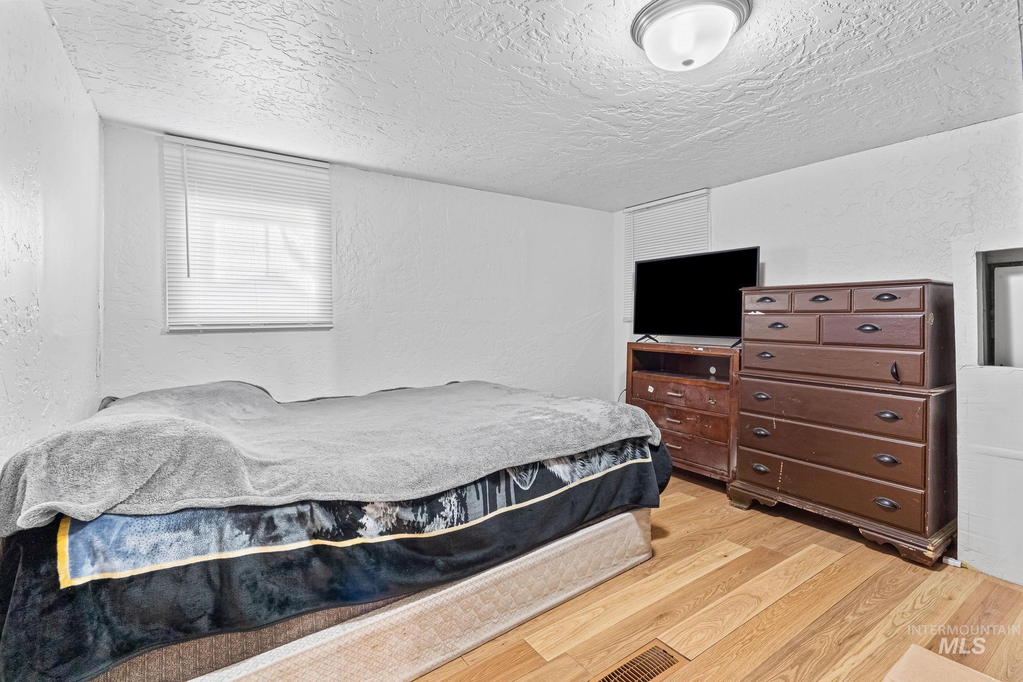 Bedroom featuring a textured wall, light wood finished floors, and a textured ceiling