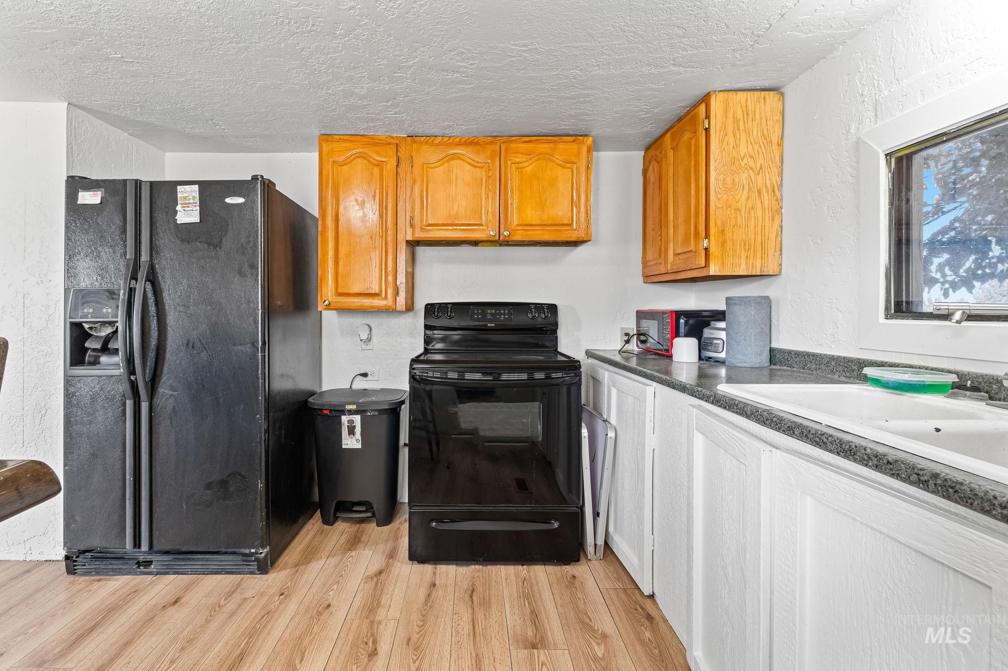 Kitchen with black appliances, light wood-style flooring, a textured ceiling, brown cabinetry, and a textured wall