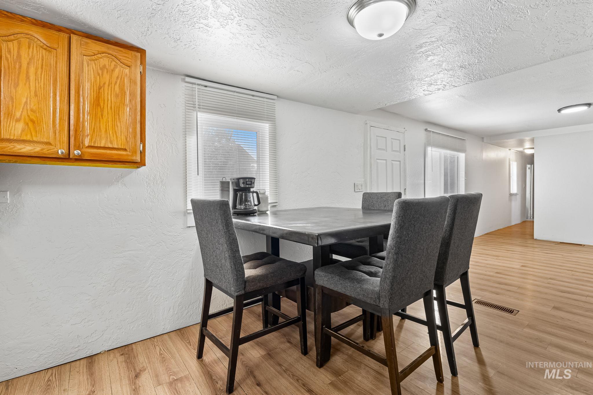 Dining area with a textured ceiling, a textured wall, and light wood-type flooring