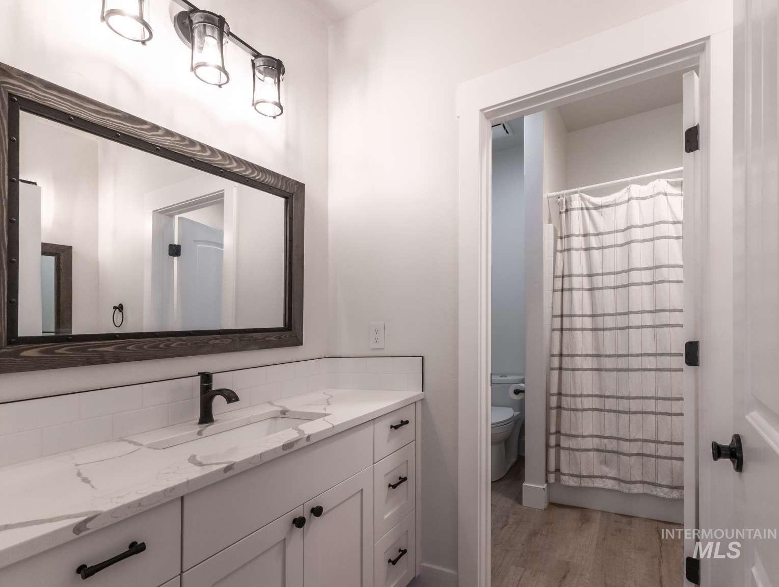 Bathroom with wood finished floors, vanity, decorative backsplash, and curtained shower