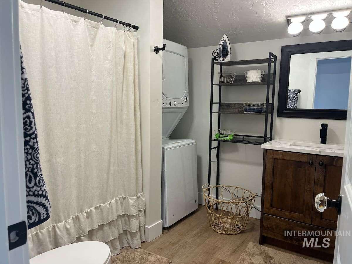 Full bathroom with estacked washer and dryer, wood finished floors, vanity, a textured ceiling, and a shower with curtain