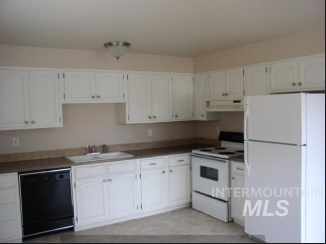 Kitchen featuring white appliances, under cabinet range hood, white cabinets, and dark countertops