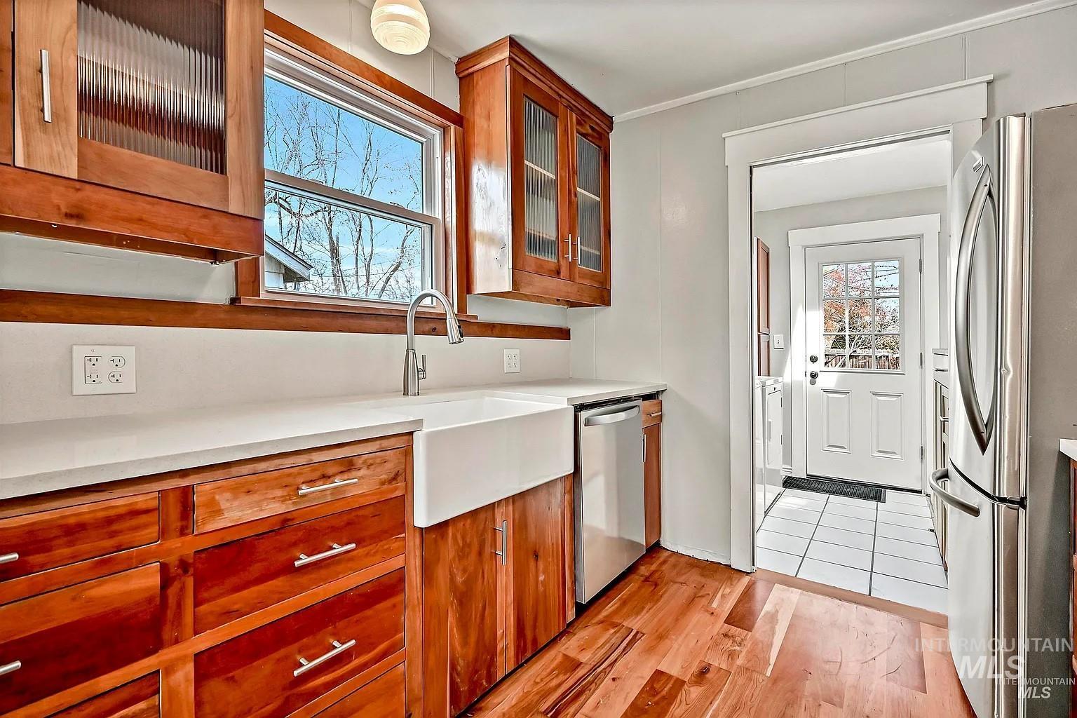 Kitchen with appliances with stainless steel finishes, light wood-style flooring, light countertops, brown cabinets, and glass insert cabinets