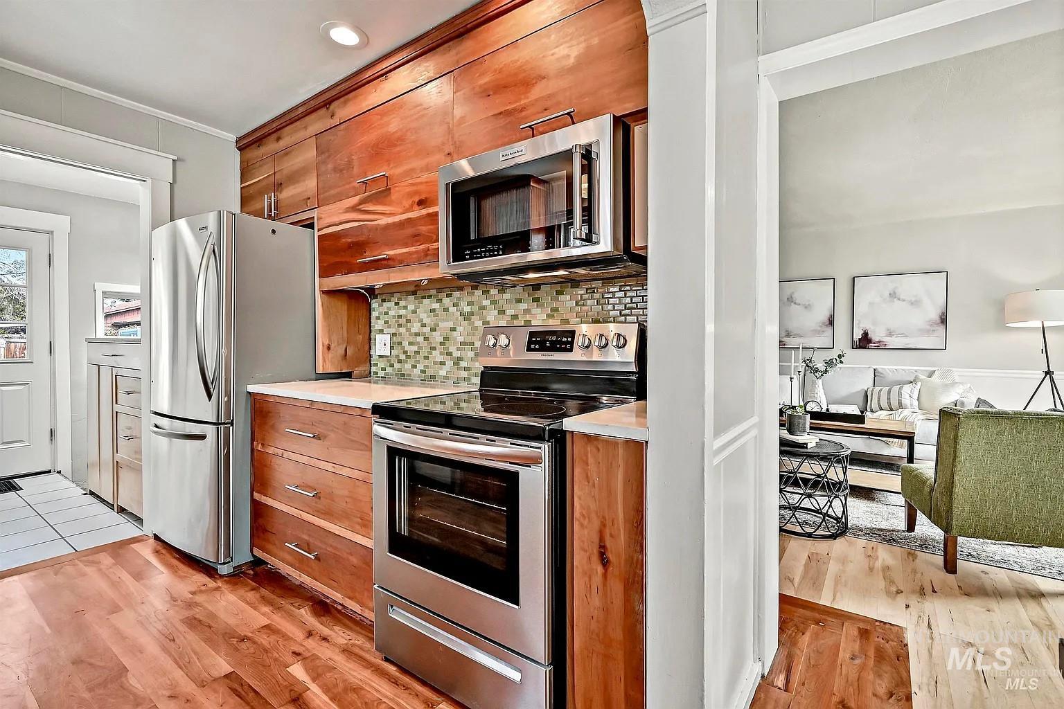 Kitchen featuring stainless steel appliances, brown cabinetry, light wood finished floors, ornamental molding, and recessed lighting