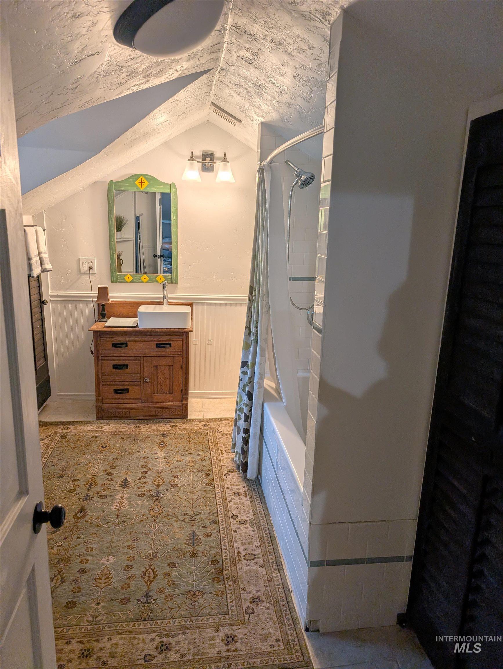 Full bath with vanity, wainscoting, shower / tub combo, and lofted ceiling