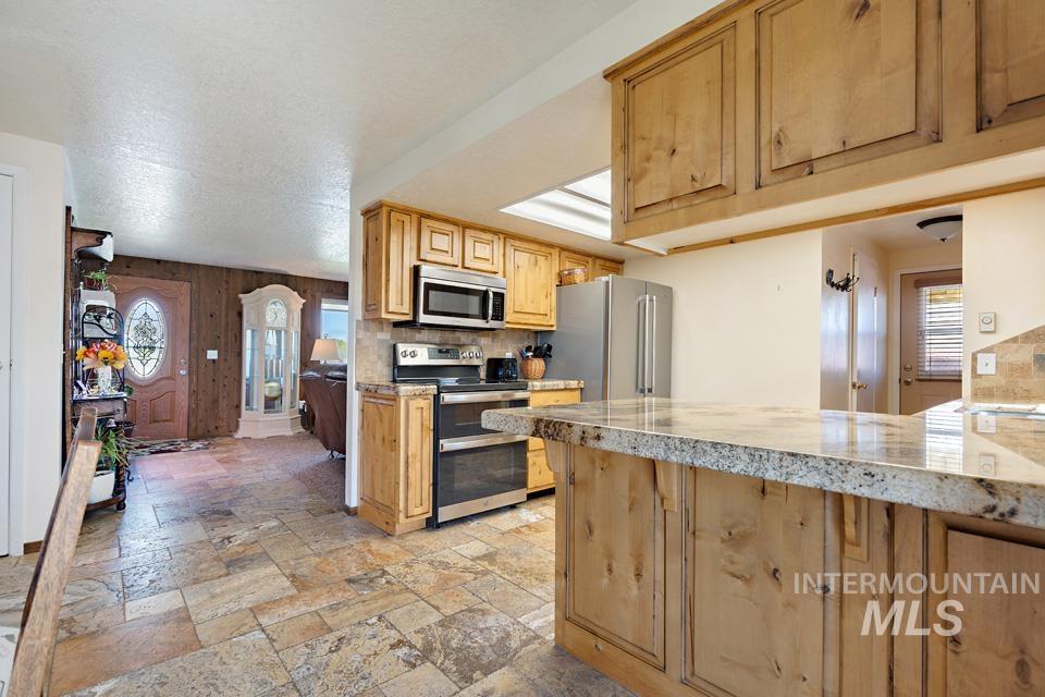 Kitchen with stainless steel appliances, stone tile floors, decorative backsplash, light stone countertops, and wood walls
