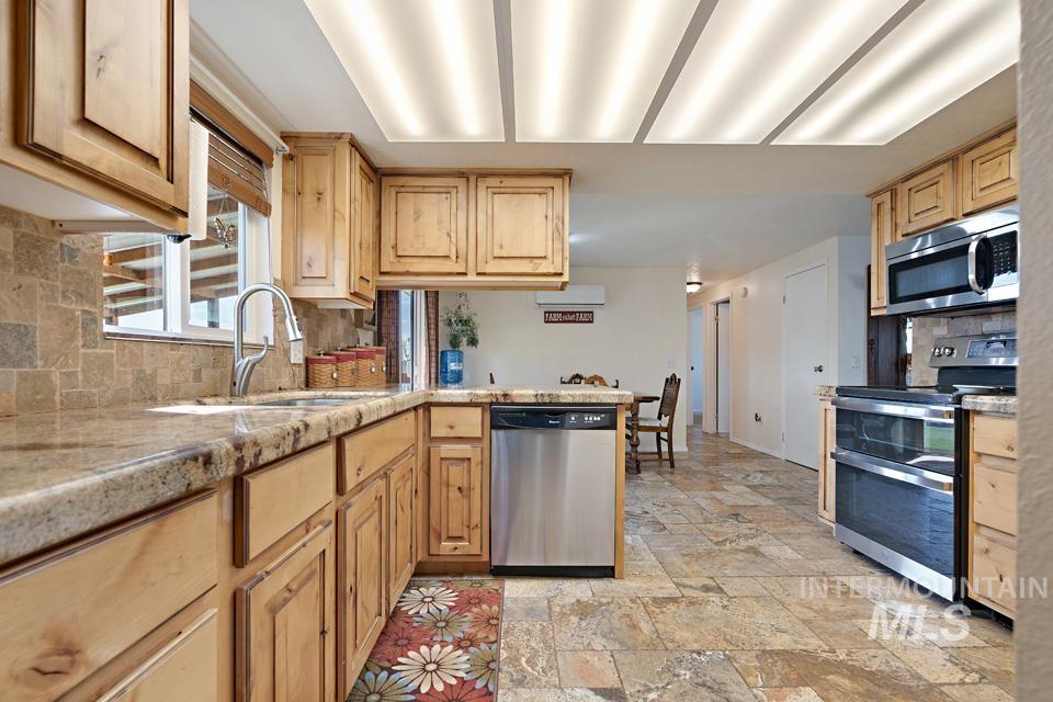 Kitchen with appliances with stainless steel finishes, backsplash, stone tile flooring, and a peninsula