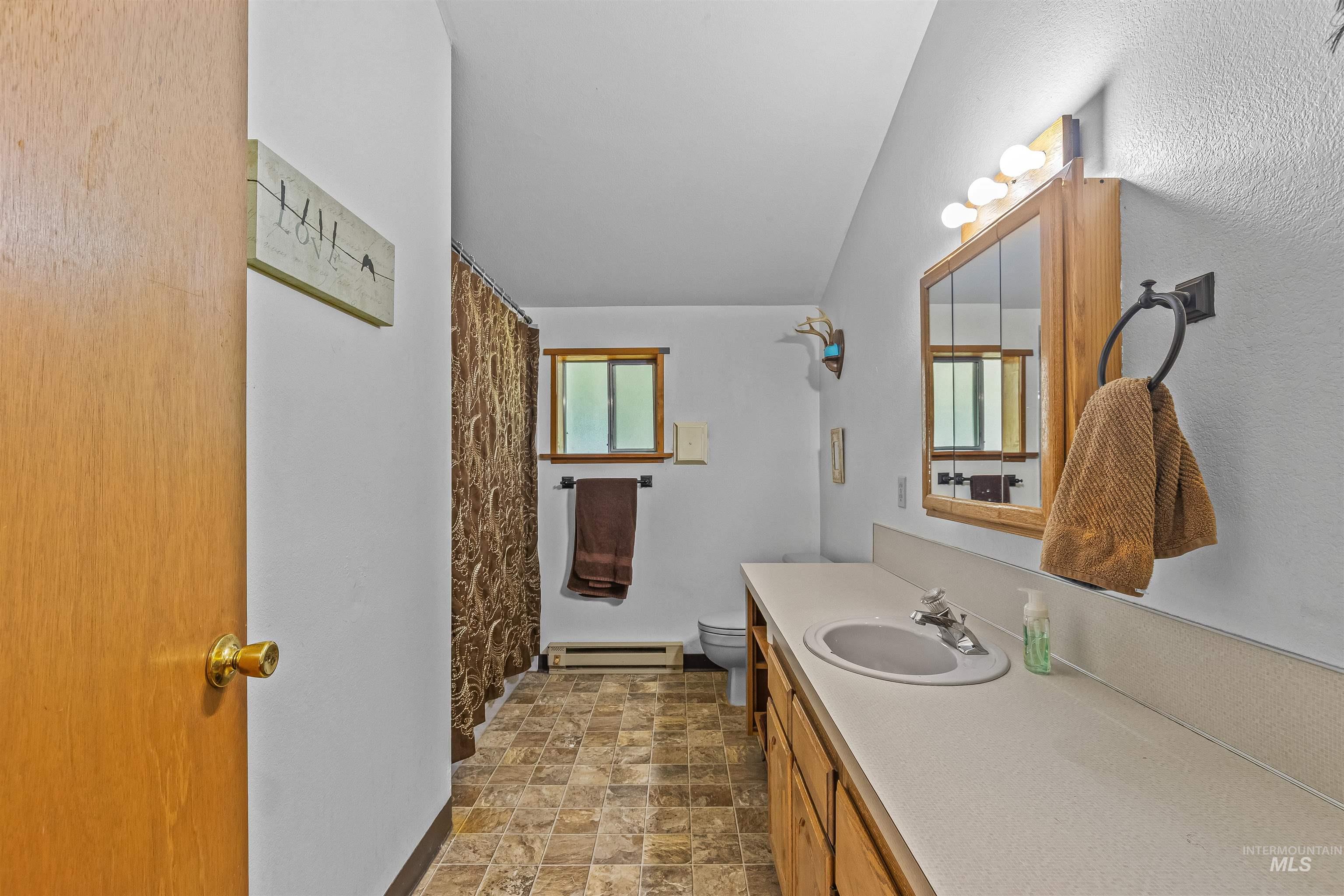 Bathroom with a baseboard radiator, vanity, stone finish floors, and a shower with curtain