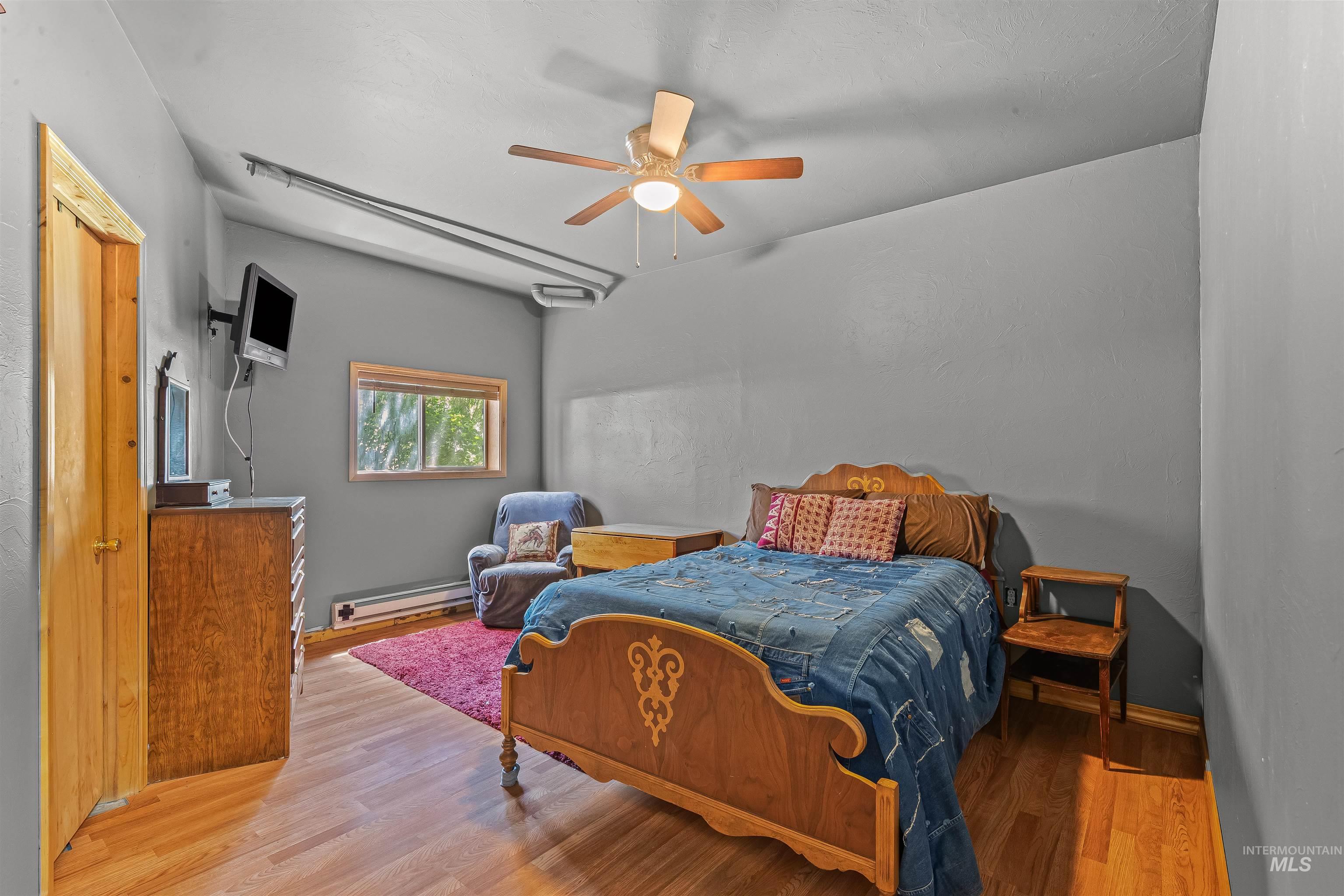 Bedroom with wood finished floors, a baseboard radiator, and ceiling fan