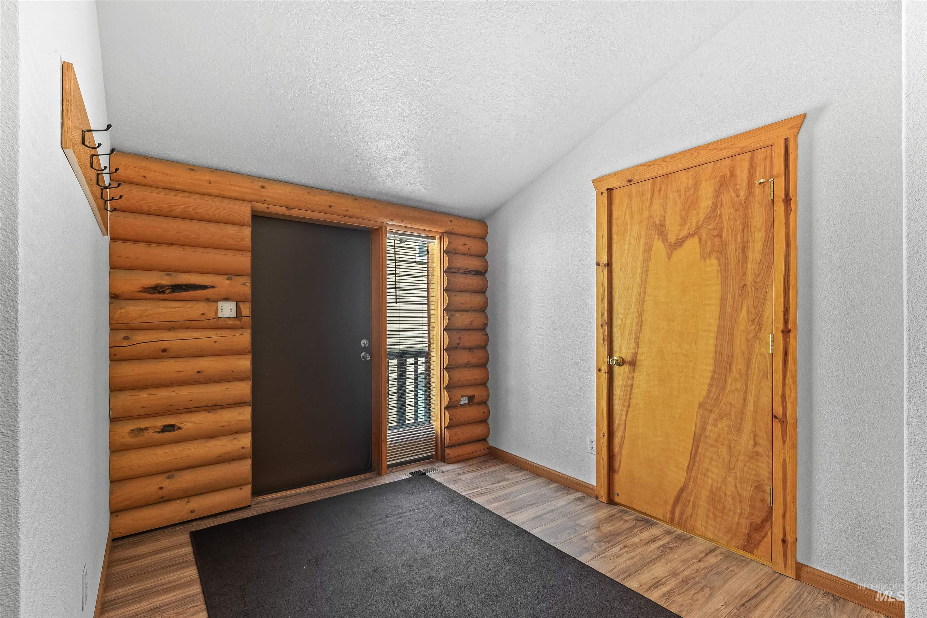 Entryway featuring wood finished floors, log walls, a textured ceiling, and lofted ceiling