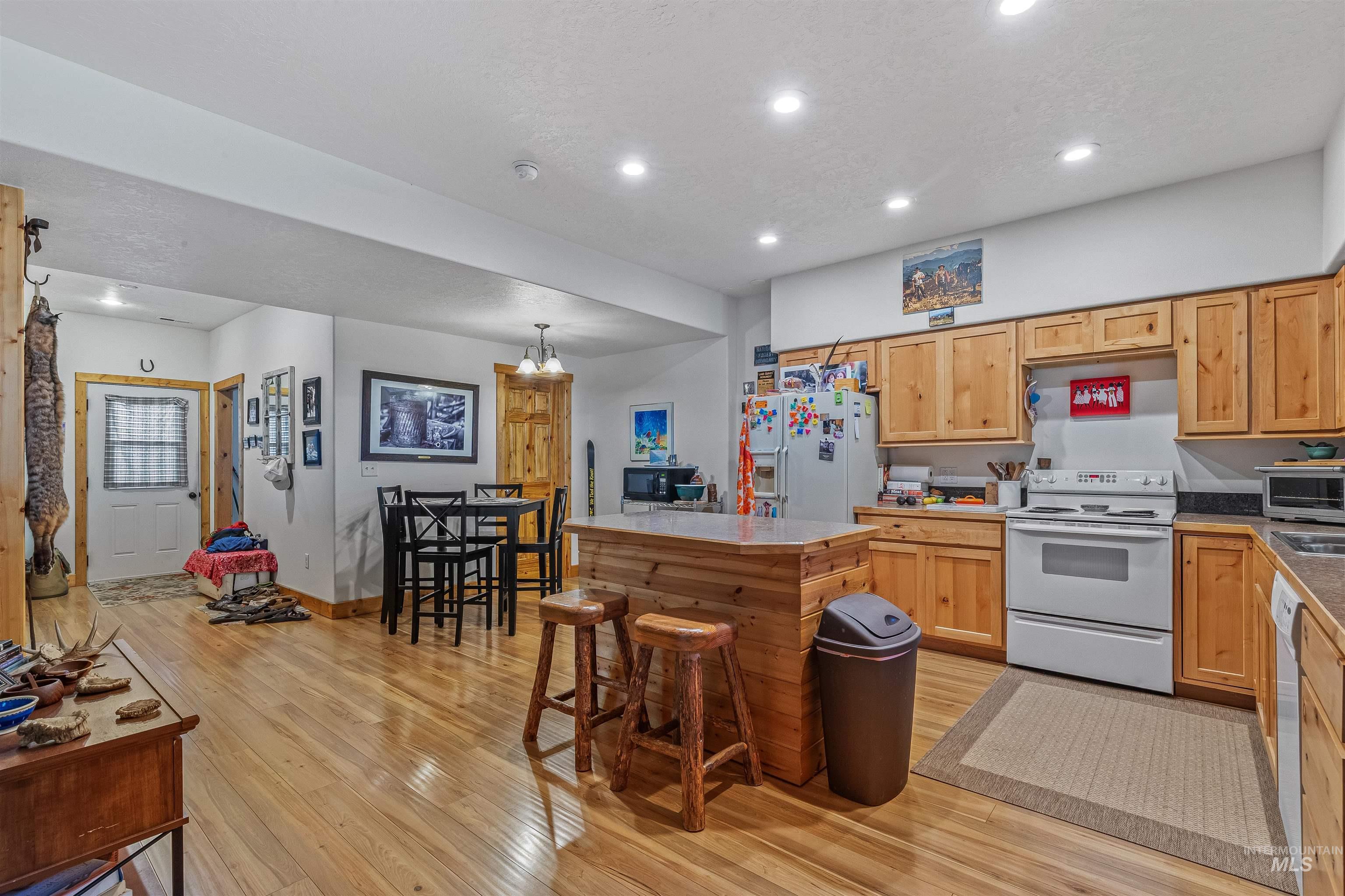Kitchen with white appliances, light wood-style floors, recessed lighting, a center island, and a breakfast bar