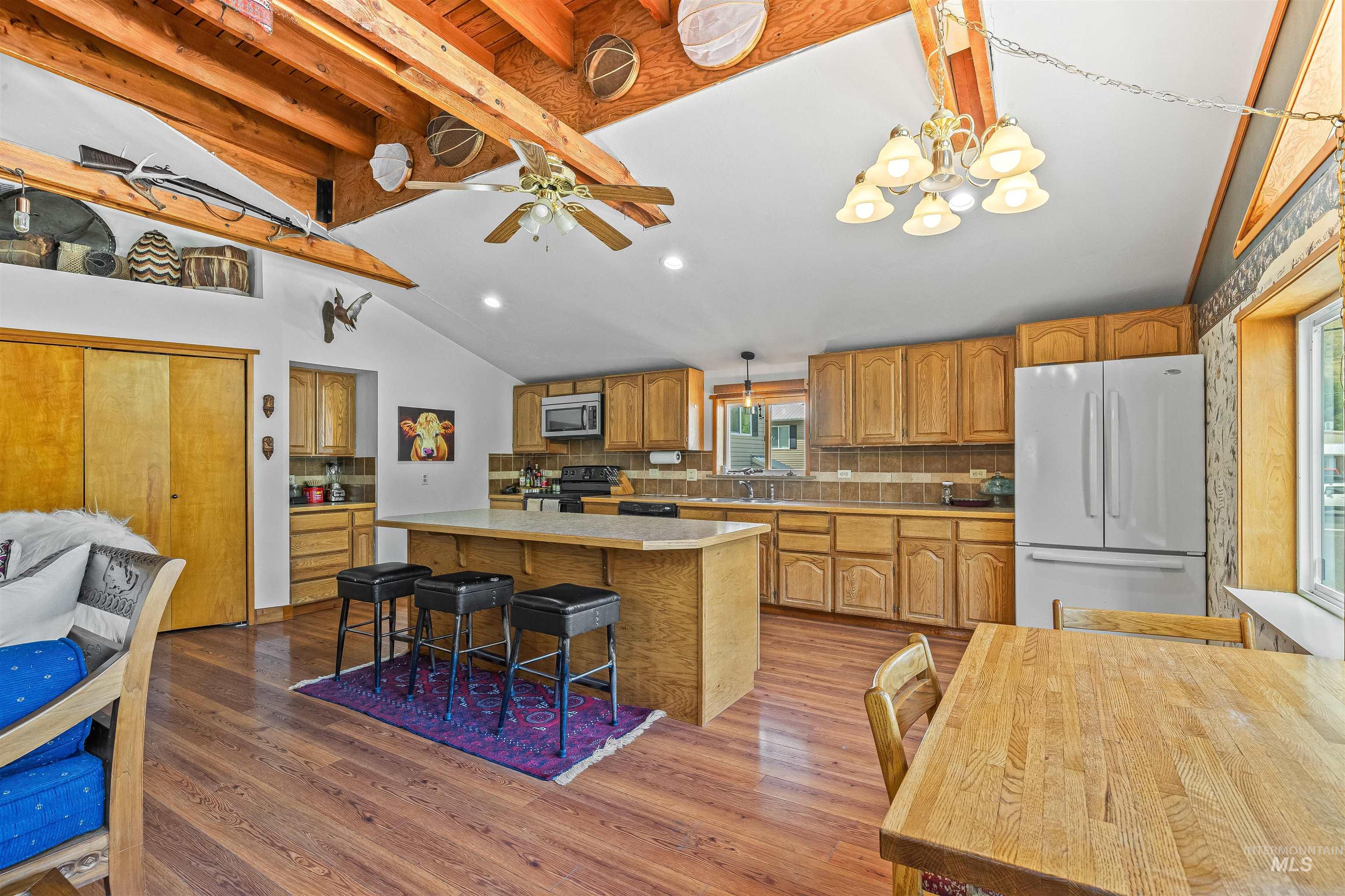 Kitchen with freestanding refrigerator, stainless steel microwave, electric range, backsplash, and wood finished floors