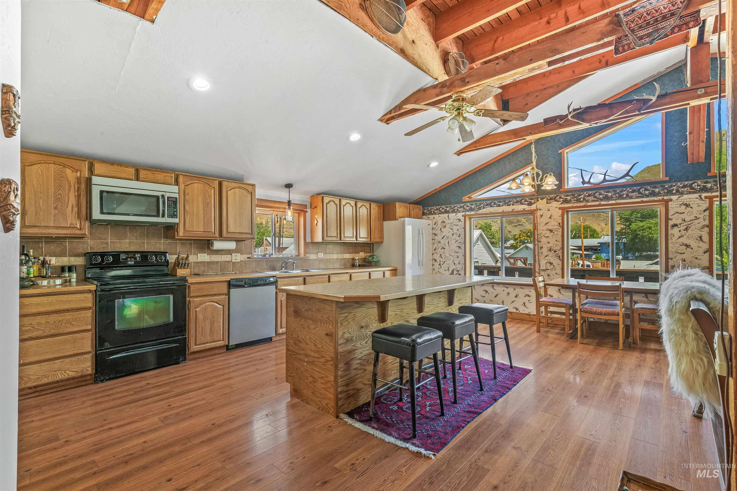 Kitchen with appliances with stainless steel finishes, light countertops, a kitchen island, light wood-style flooring, and beamed ceiling