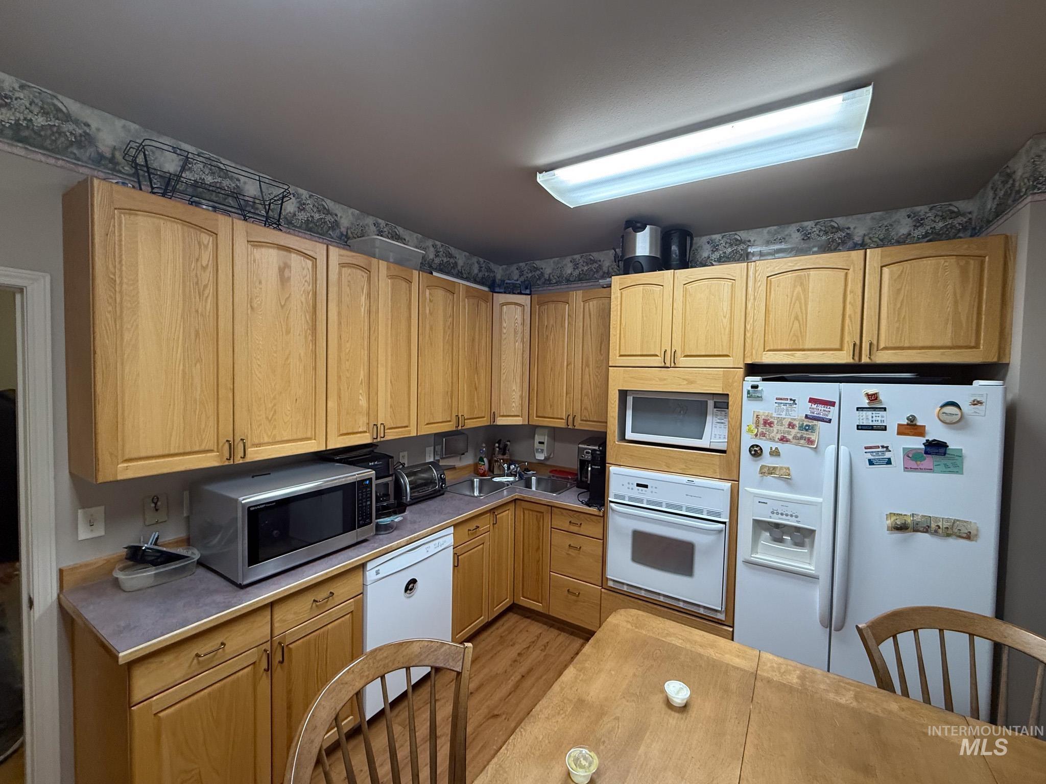 Kitchen with white appliances, light wood-style flooring, and light countertops