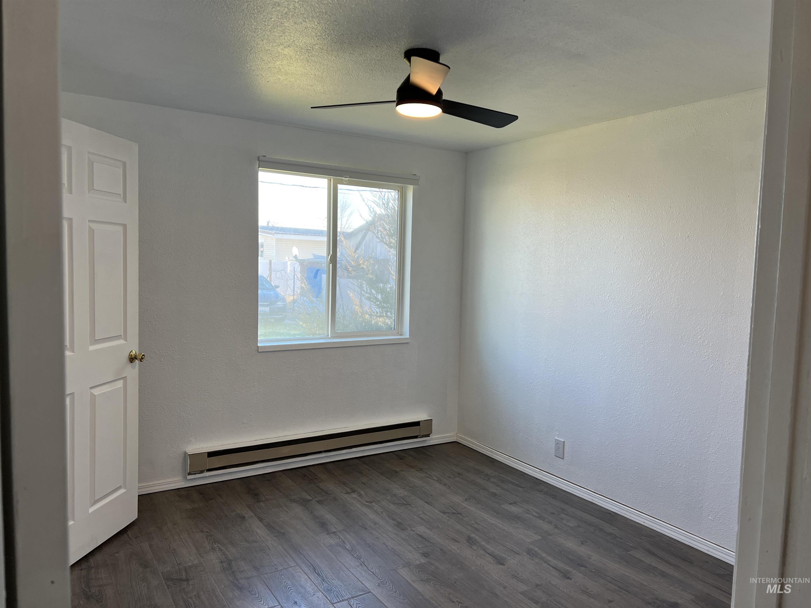 Spare room featuring a baseboard heating unit, a ceiling fan, and dark wood-type flooring