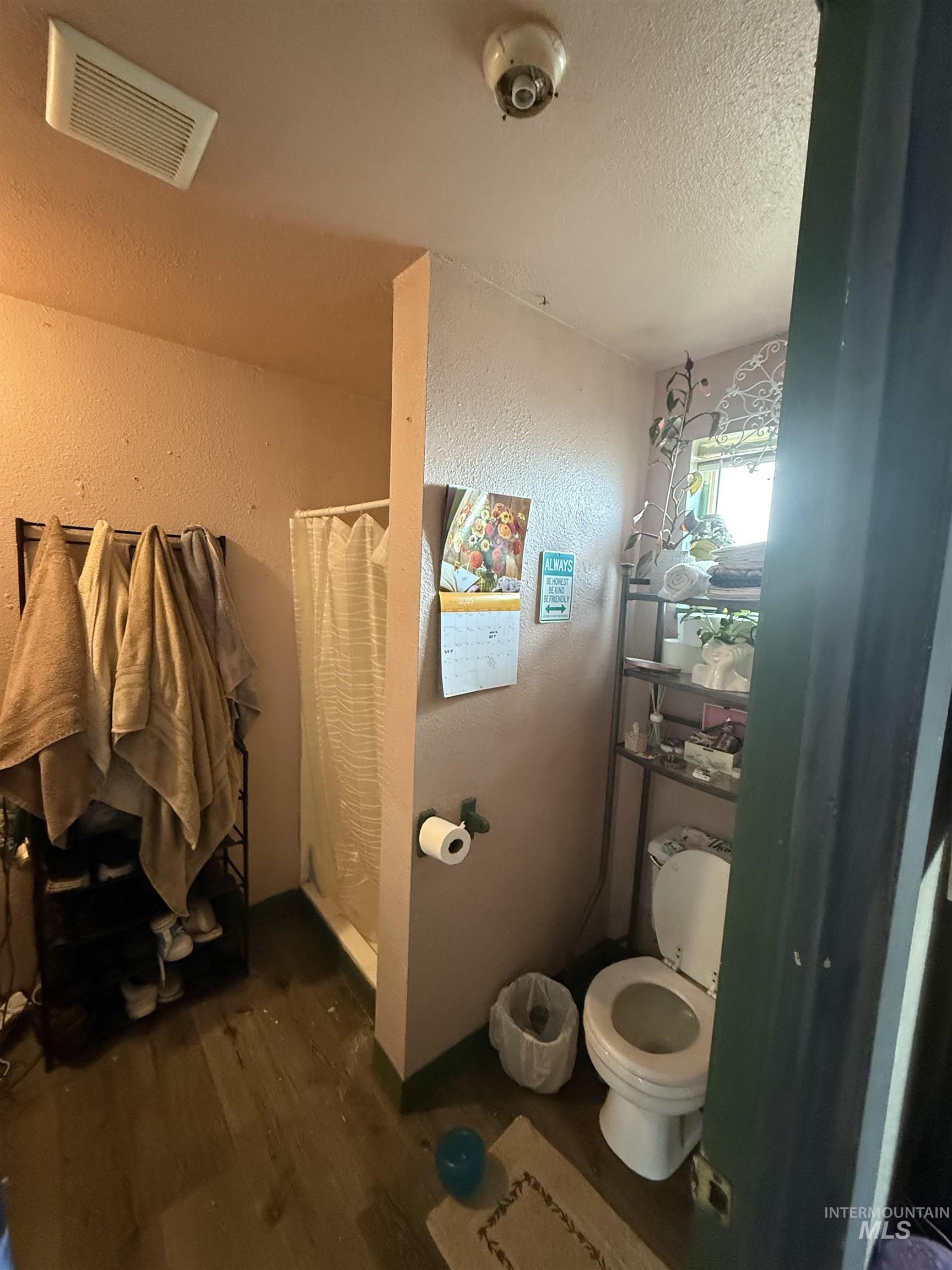 Bathroom featuring wood finished floors, a shower with curtain, a textured ceiling, and a textured wall