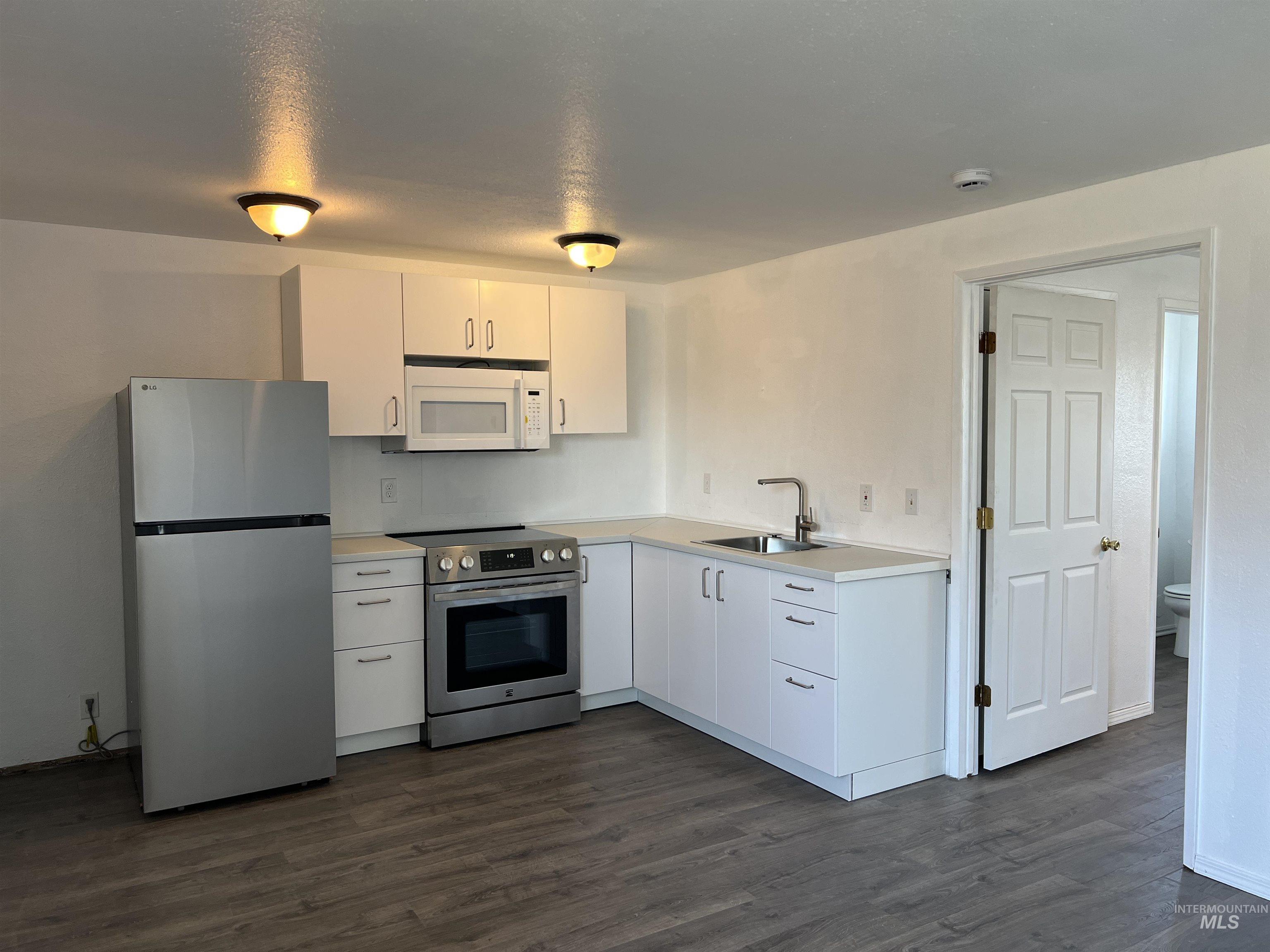 Kitchen featuring appliances with stainless steel finishes, light countertops, dark wood-type flooring, and white cabinetry