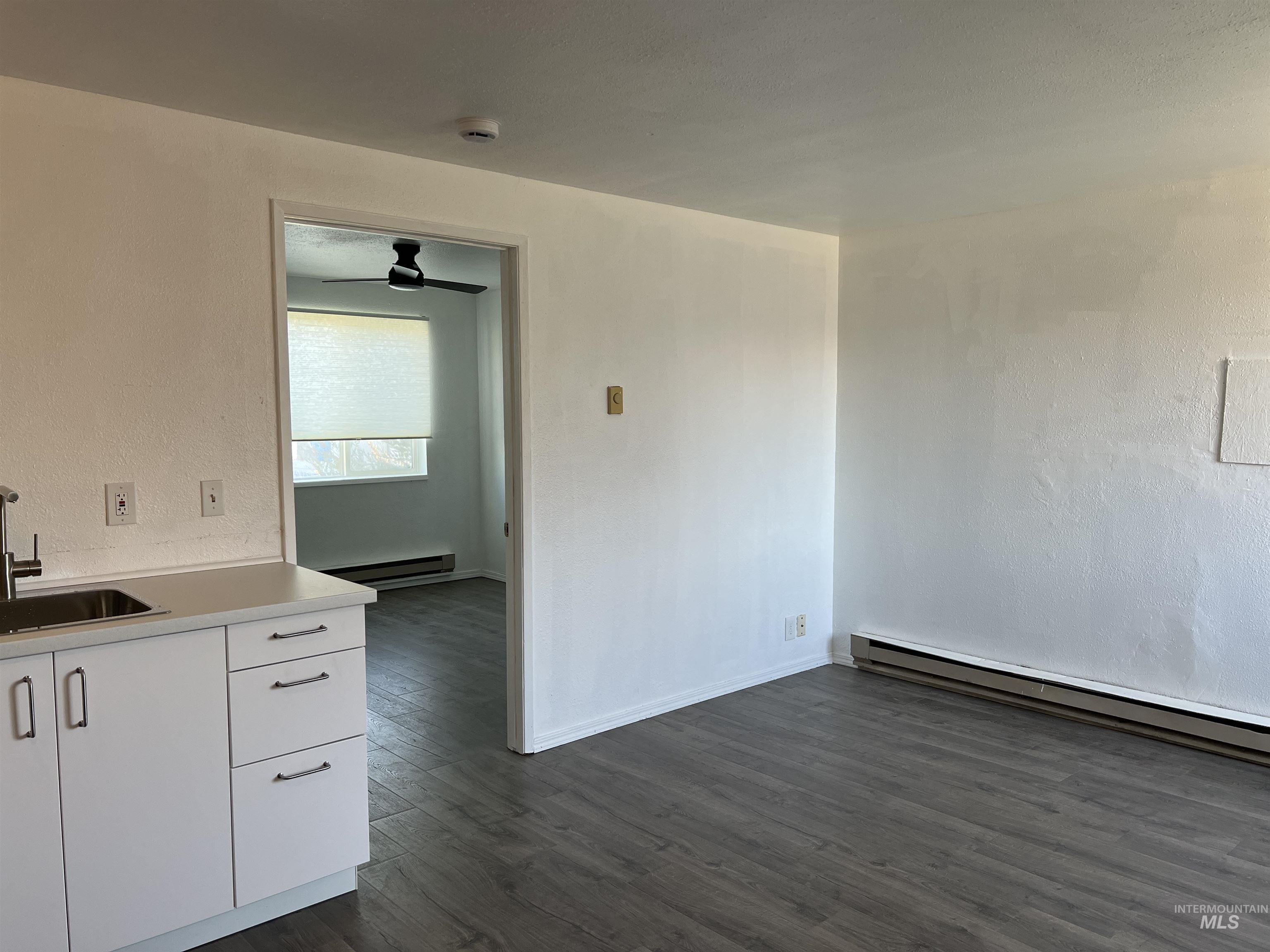 Unfurnished dining area with baseboard heating, dark wood-style flooring, and ceiling fan